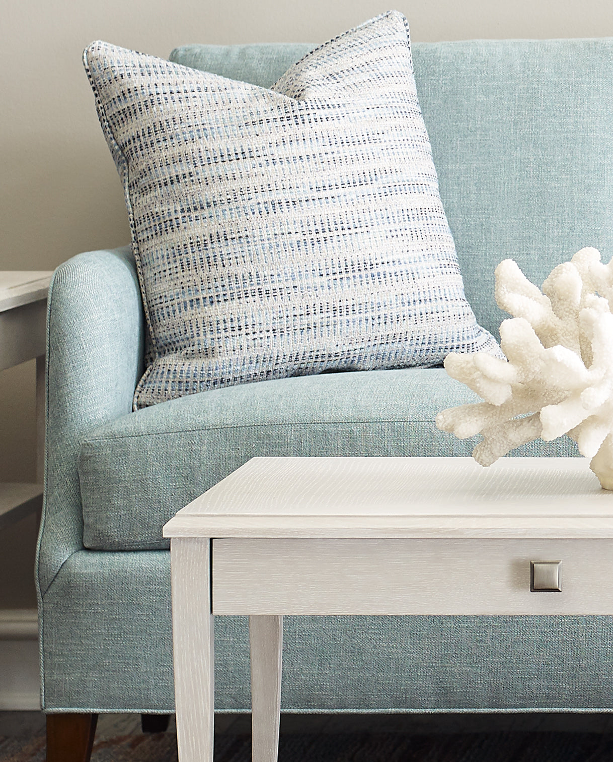 A closeup of a blue fabric couch with a plush blue and white decorative pillow.